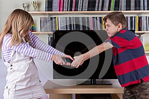 Siblings fighting desperatelly for the TV remote control in front of the televison