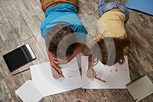 Siblings friendship. Top view of little caucasian brother and sister lying on the wooden floor at home and drawing