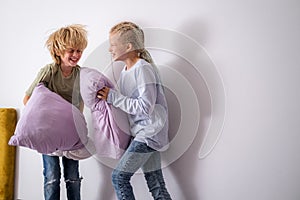 siblings having fun, laughing, boy and girl play pillow fight in messy childrens room, kids playing among the many toys