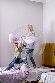 siblings having fun, laughing, boy and girl play pillow fight in messy childrens room, kids playing among the many toys