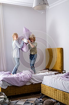 siblings having fun, laughing, boy and girl play pillow fight in messy childrens room, kids playing among the many toys