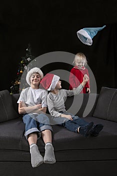 Siblings at home on the sofa on Christmas Eve. Happy children play and throw up their hats