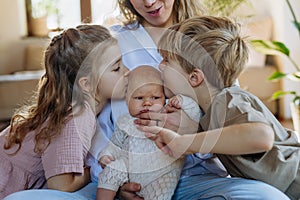 Siblings kissing the cheeks of a little baby. Big brother and big sister meeting newborn sister, enjoying together time.