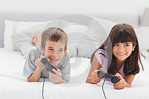 Siblings lying on bed playing video games