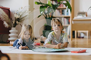 Siblings lying on stomach and painting at home with watercolors, markers and tempera paints, creating a model of planet