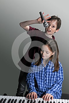 Siblings making music the girl plays keyboard and the boy sings a song