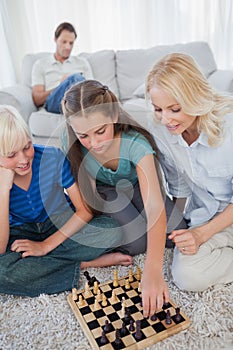 Siblings and mother playing chess sitting on a carpet