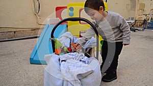 Siblings outdoors - cute two years old boy playing with pegs for clothes and giving them to his baby brother in carry cot