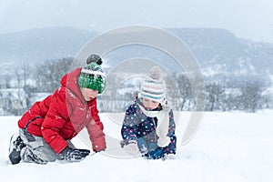 Siblings outside in the snowy day. Two children play and sitting on the snow on frosty winter day. Winter holidays