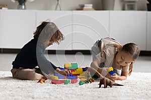 Siblings play cubes and dinosaurs sit on floor at home