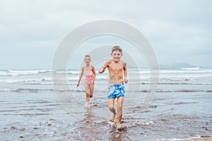 Siblings playing on beach, running, skipping, having fun. Smilling girl and boy on sandy beach of Canary islands