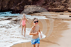 Siblings playing on beach, running, skipping, having fun. Smilling girl and boy on sandy beach of Canary islands