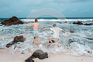 Siblings playing on beach, running, skipping rocks. Smilling girl and boy ion sandy beach with volcanic rocks of Canary
