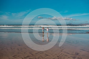 Siblings playing on beach, running, skipping in water. Smilling girl and boy on sandy beach of Canary islands. Concept