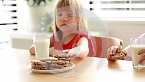 Siblings share a moment of joy eating cookies and drinking milk at the table