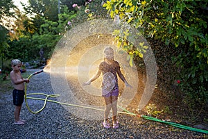 Siblings sharing laughter with a water hose on a sunny summer day.
