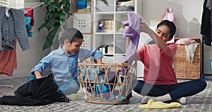 Siblings sit on the laundry room floor sorting colored clothes before putting them in the washing machine, doing