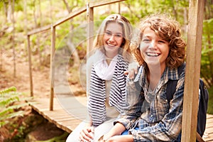 Siblings sitting on a wooden bridge in a forest, portrait
