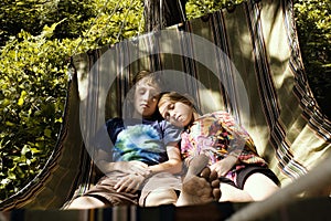 Siblings sleeping on a hammock over lush undergrowth