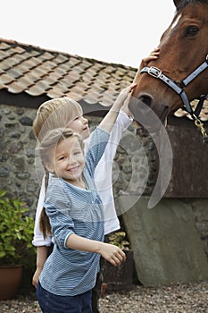 Siblings Stroking Horse Outside Stable