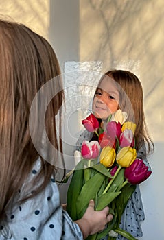 Siblings or twin day. Women& x27;s or Mother& x27;s Day. Portrait of two smiling little girl with a bouquet of tulips