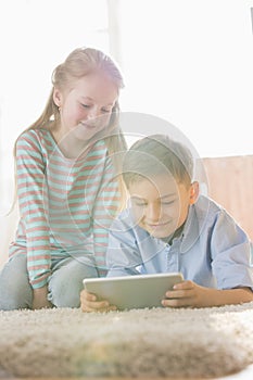 Siblings using digital tablet on floor at home