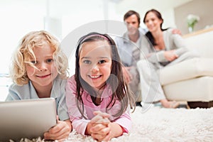 Siblings using a tablet computer while their parents are in the