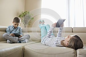 Siblings using technologies on sofa at home