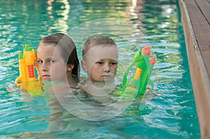 The siblings with a water pistols playing in a pool