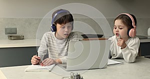 Siblings wearing headphones studying online from home by video call