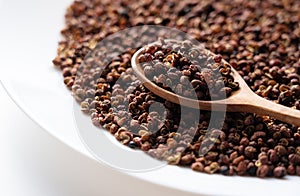 Sichuan pepper, wooden spoon and plate set against a white background