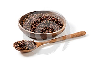 Sichuan pepper, wooden spoon and plate set against a white background