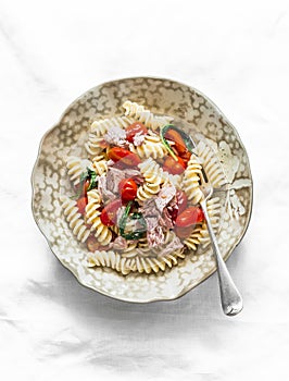 Sicilian fusilli pasta with canned tuna, cherry tomatoes and spinach on a light background, top view