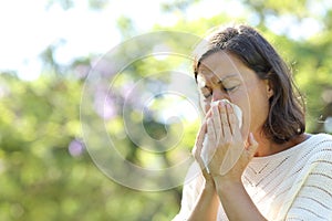 Sick adult woman blowing nose with tissue in the park