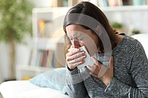 Sick adult woman coughing covering mouth with tissue at home