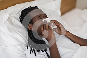 Sick African American Man Blowing Nose In Tissue While Lying In Bed