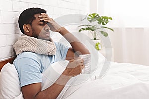 Sick african-american man drinking hot healing tea in bed