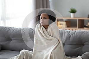 Sick african woman feeling cold covered with blanket at home