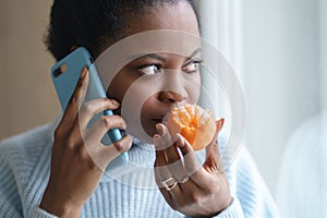 Sick afro woman trying to sense smell of half fresh tangerine orange talking on phone. Covid-19