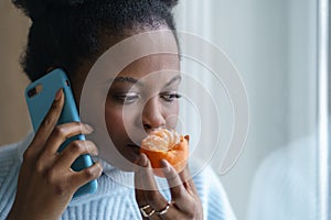 Sick afro woman trying to sense smell of half fresh tangerine orange talking on phone. Covid-19