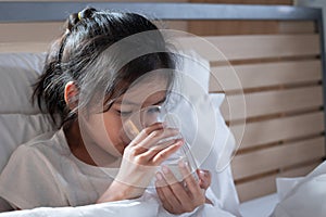 Sick asian child girl is drinking water from a glass after eat medicine in bedroom.