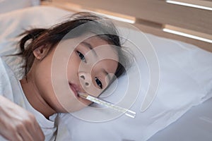 Sick asian child girl is sleeping on bed and measuring her body temperature with thermometer in the bedroom