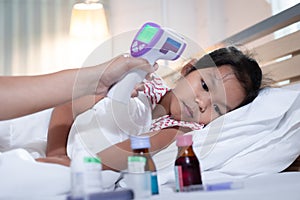 Sick asian child girl is sleeping and mother is checking up and measuring her body temperature with contactless thermometer