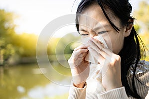 Sick asian child girl sneezing in a tissue blowing her runny nose,hay fever,female teen with blocked nose,weather is changing,