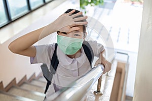 Sick asian child girl touching her forehead,checking the temperature,illness and fever,schoolgirl wear face mask has flu and cold