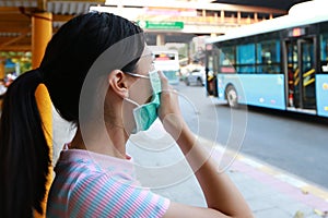 Sick asian child girl wearing protection mask against air pollution at bus stop in the city Bangkok,inhale fine dust,pm 2.5,female