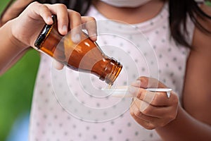 Sick asian little child girl pouring liquid medicine into spoon