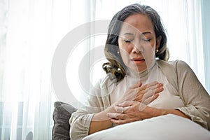 A sick Asian middle-aged woman with heart disease or heart ache, touching her chest