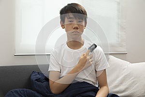 Sick asian teen boy with pulse oximeter on his finger. Ill child lying on sofa with blanket.