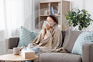 Sick asian woman blowing nose with tissue at home